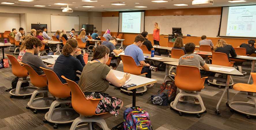 Photo of a Case Western Reserve University classroom with students seated at rows of tables and orange chairs