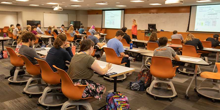 Photo of a Case Western Reserve University classroom with students seated at rows of tables and orange chairs