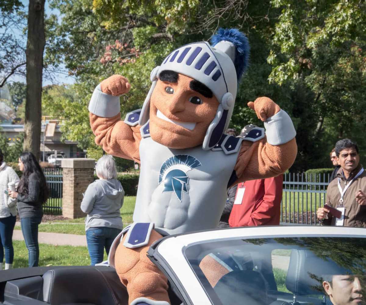 Photo of Case Western Reserve University Spartan mascot, Spartie, flexing muscles while riding in a car in the homecoming parade