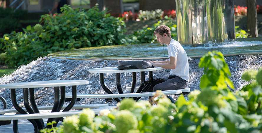 Photo of a Case Western Reserve University student sitting at a picnic table next to Michelson-Morley fountain