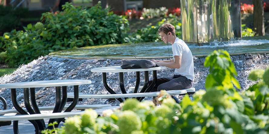 Photo of a Case Western Reserve University student sitting at a picnic table next to Michelson-Morley fountain