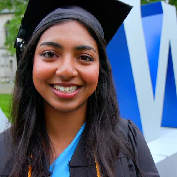One woman student smiling for the camera in front of a CWRU sign on campus.