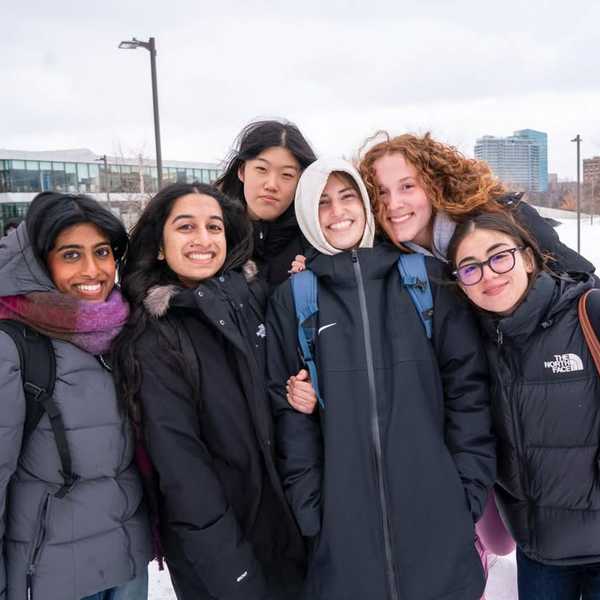 A group of six students bundled up in winter coats on campus.