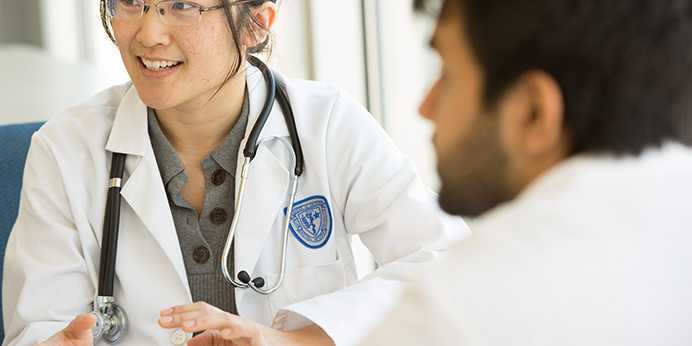 Photo of two Case Western Reserve University School of Medicine students wearing white coats engaging in discussion