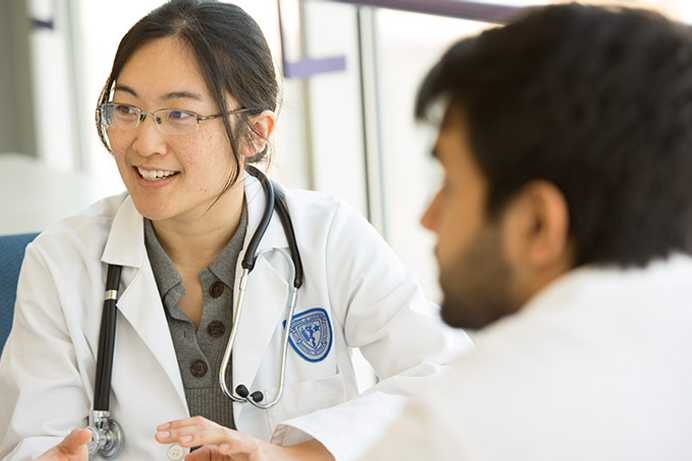 Photo of two Case Western Reserve University School of Medicine students wearing white coats engaging in discussion