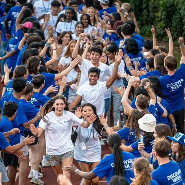 Two lines of students, one of orientation leaders and the other of first-year students, high-five in blue CWRU gear on DiSanto Field during orientation.
