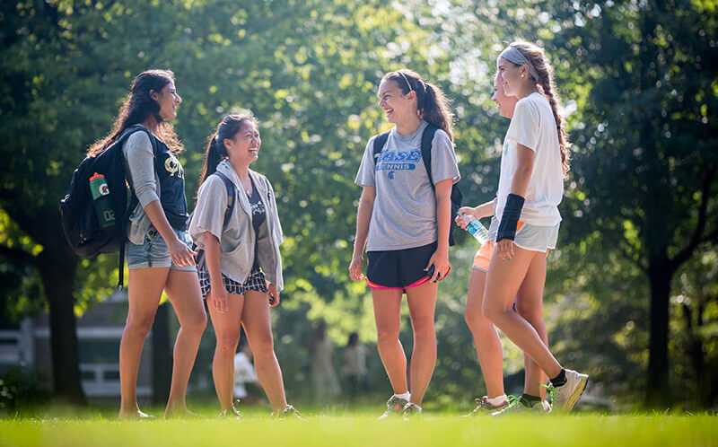 Photo of a group of Case Western Reserve University students standing in a circle outdoors on the quad, laughing
