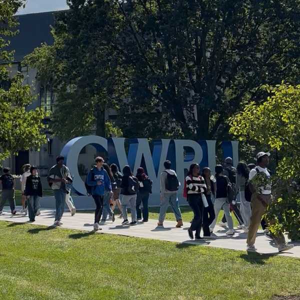 A large group of students walking in front of a large gray and blue sign that spells, “CWRU.”