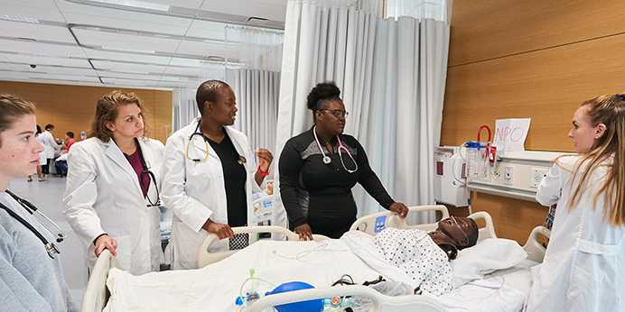 Photo of Case Western Reserve University nursing students surrounding a hospital bed with a manikin patient