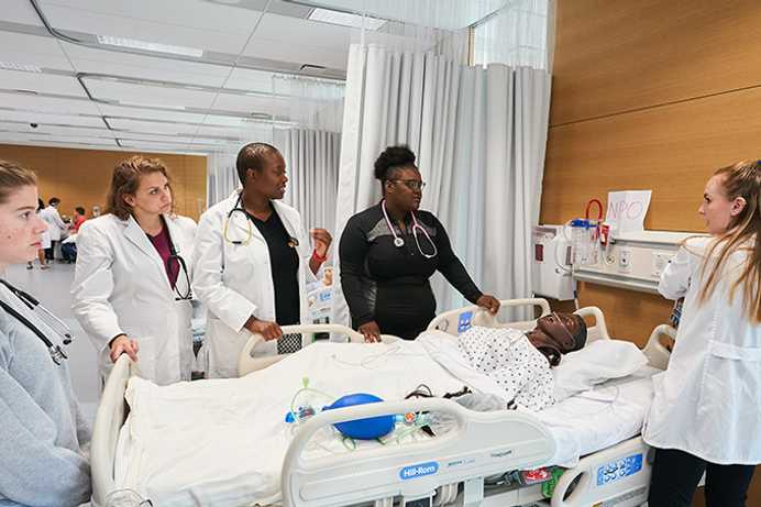 Photo of Case Western Reserve University nursing students surrounding a hospital bed with a manikin patient