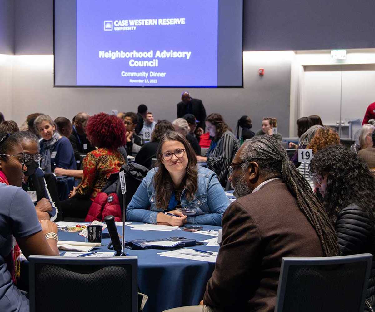 A diverse group of attendees at the Neighborhood Advisory Council's Community Dinner on Nov. 17, 2023, sit at circular tables in a conference room.