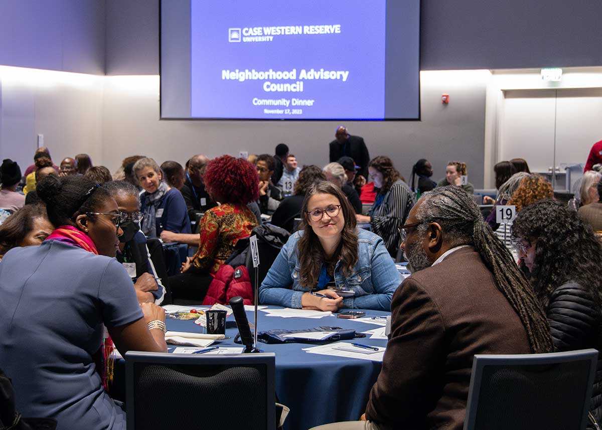 A diverse group of attendees at the Neighborhood Advisory Council's Community Dinner on Nov. 17, 2023, sit at circular tables in a conference room. 