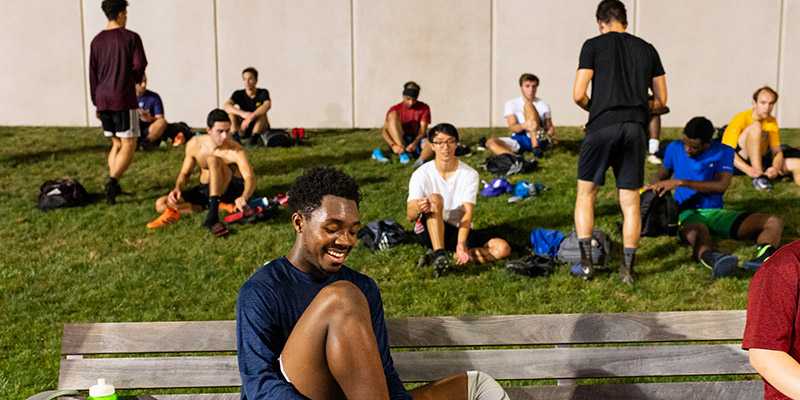 Photo of a group of college-aged athletes sitting in a grassy area getting ready for a match