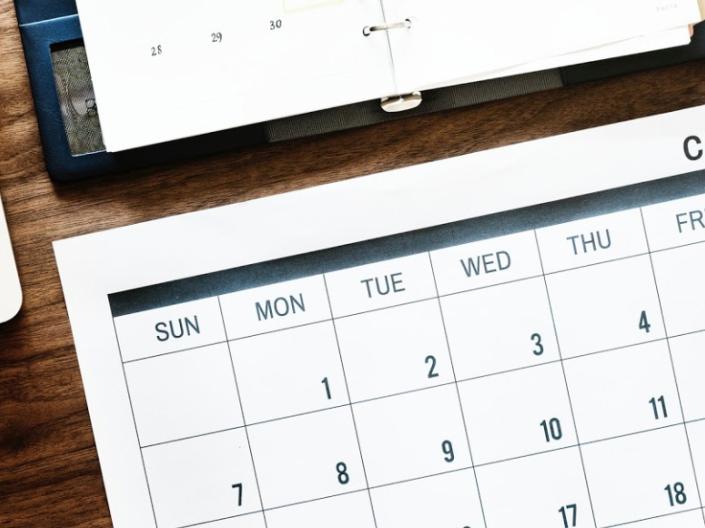 Top-down view of a printed calendar on a desk with a laptop and planner