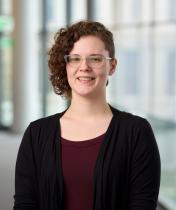 Headshot of a white woman with short curly hair wearing a black cardigan and maroon shirt