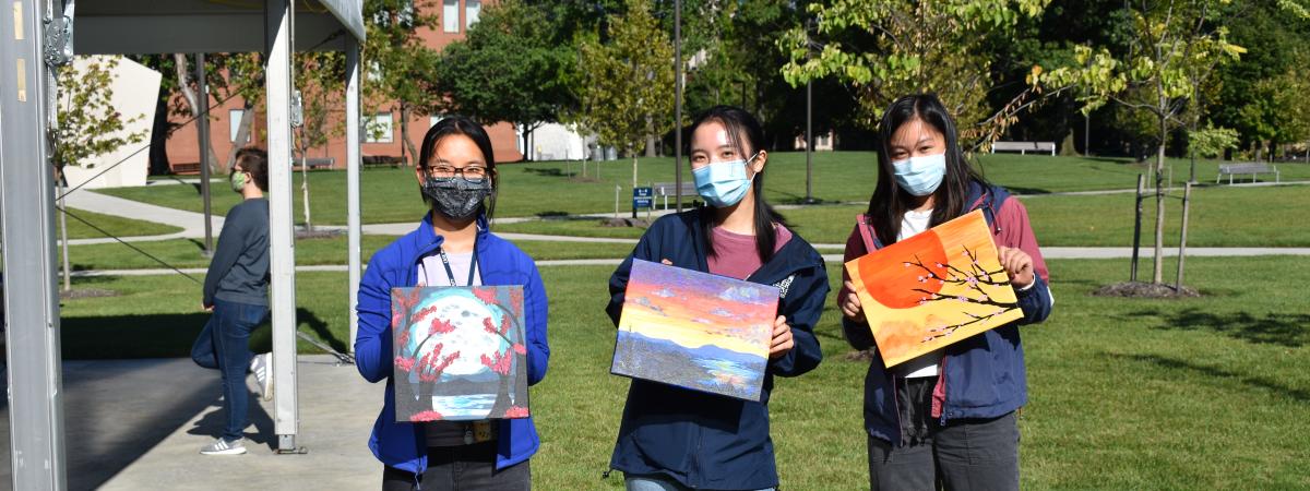 Three individuals standing and holding up their paintings from the Tiny TSO event