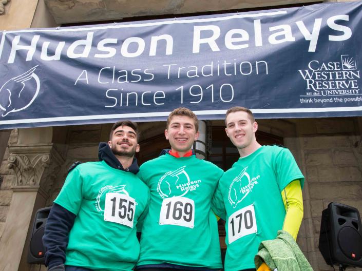Three students in front of the Hudson Relays banner on Adelbert Hall