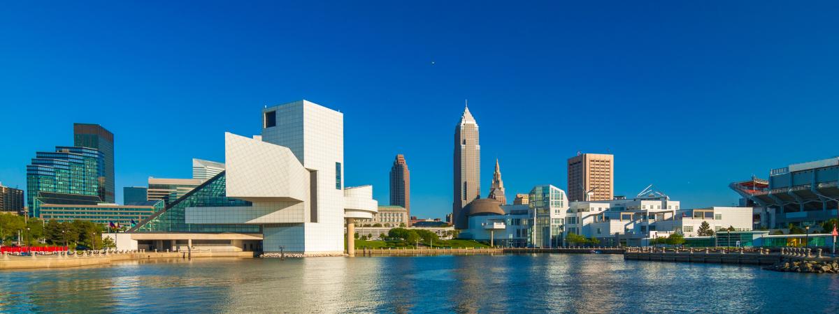 Landscape photo of large buildings reflecting off the water on a clear and sunny day in Cleveland, OH