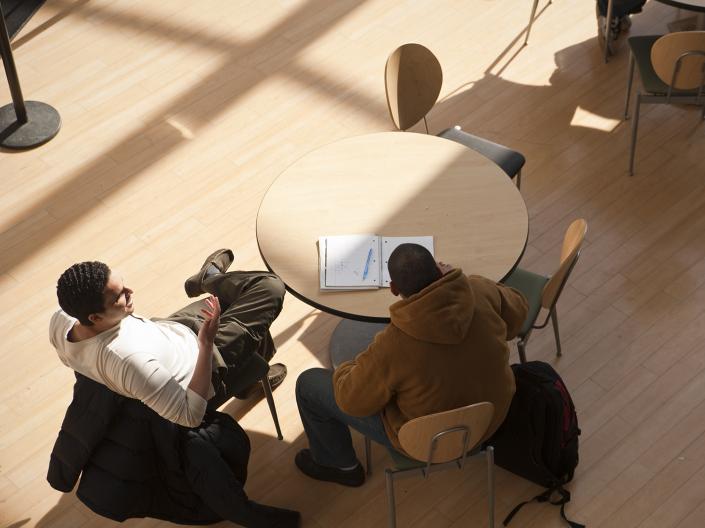 Two people sitting at a table and conversing over a textbook and papers