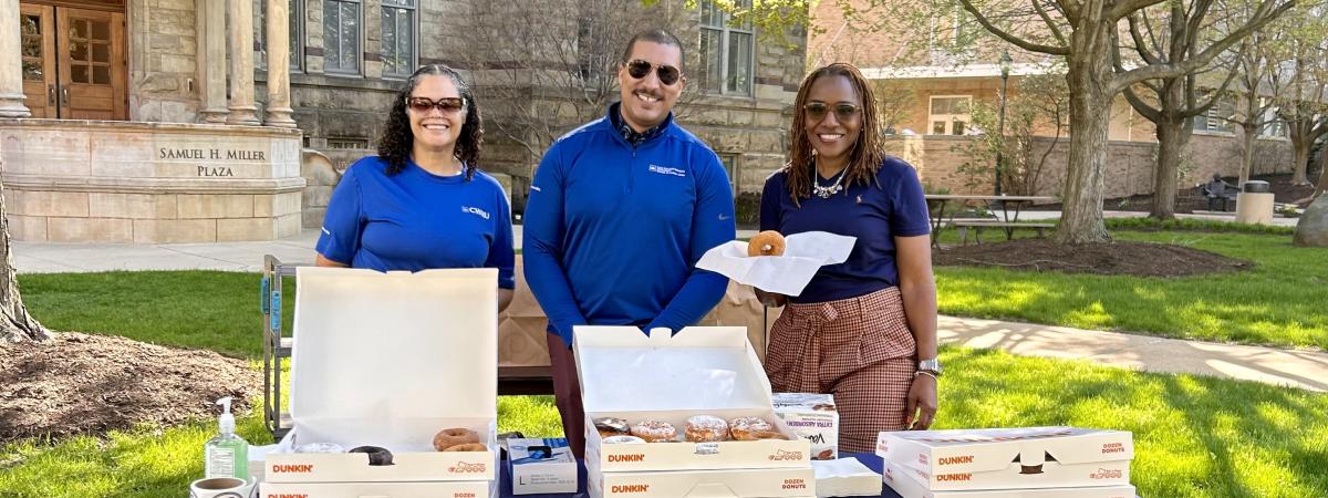 Three people standing behind a table with donuts