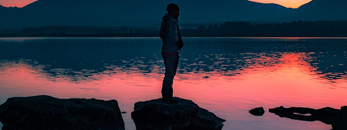 A study abroad student stands on a rock in the middle of water during sunset