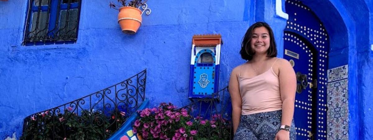 A student stands against a blue building during her study abroad