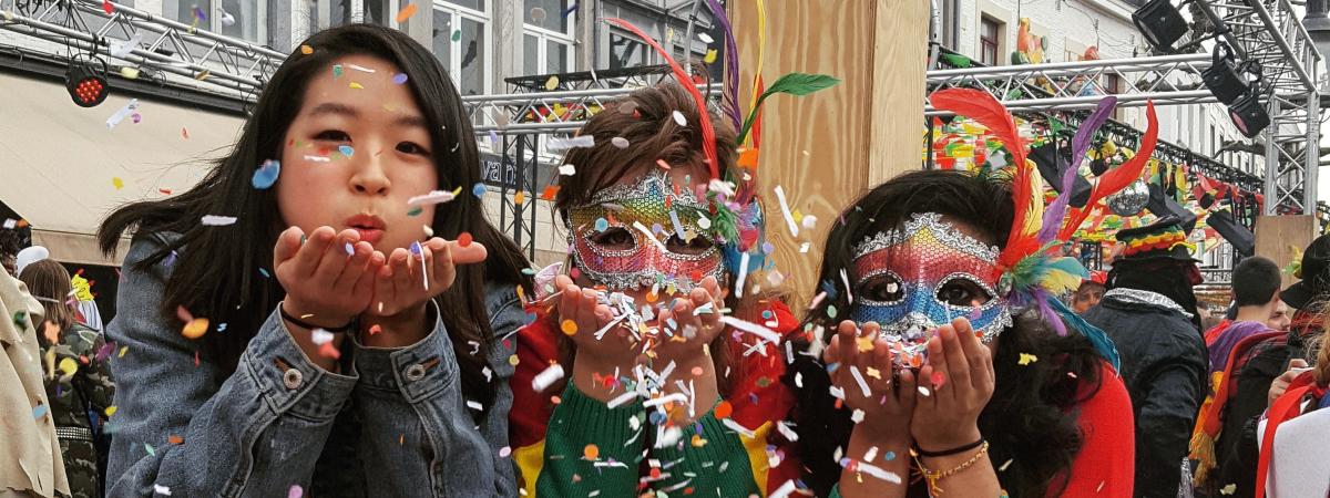 Three students blow confetti at the camera at a cultural festival