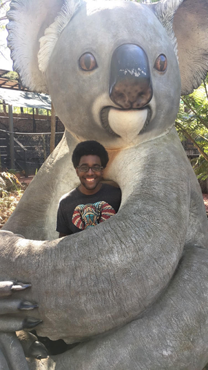 A photo of Miles Booker standing with a statue of a koala bear