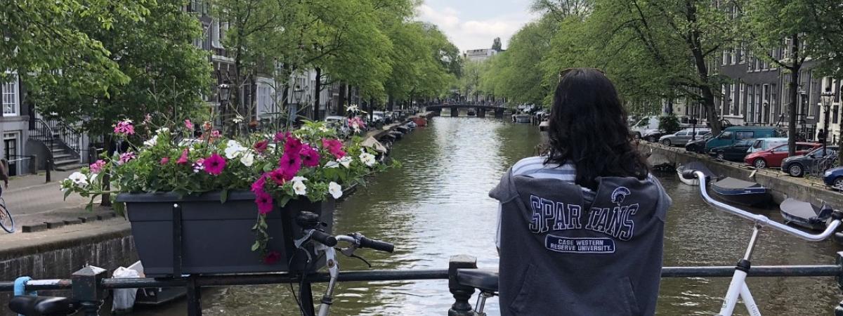 A student with a CWRU shirt on looks at a river between two rows of buildings and trees