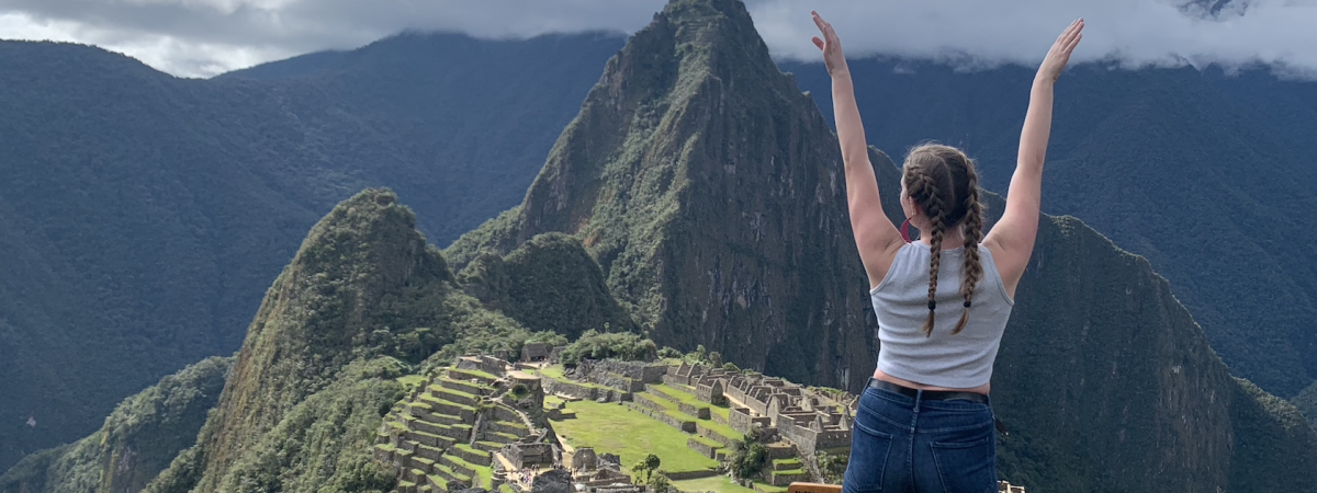 Student with arms spread wide looking away towards Macchu Piccu