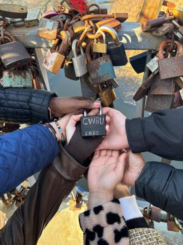 CWRU students touching hands while attaching a lock to a bridge