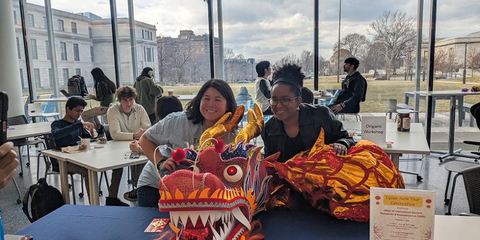 Two students smiling behind a red paper dragon at Case Western Reserve University's Lunar New Year event.