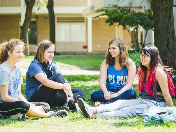 Four students sitting outside smiling