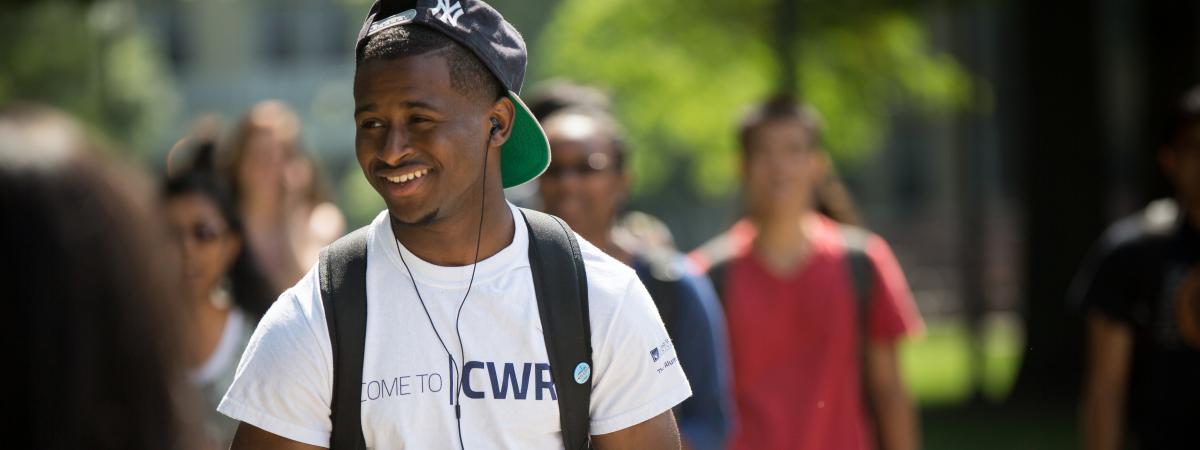 Smiling student walking outside wearing a shirt that says "Welcome to CWRU"