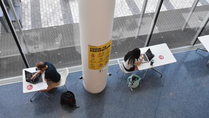 Two students with masks on sitting at tables with their computers.