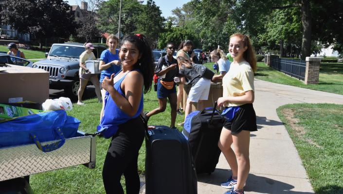 A group of students smiling outside with suitcases