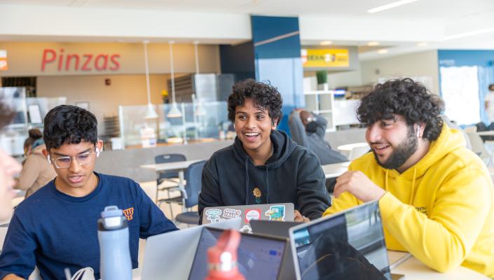 Three students smiling at a table in TVUC.
