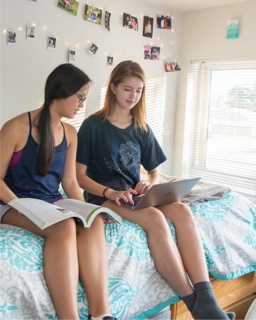 Two girls sitting on a bed in their dorm room