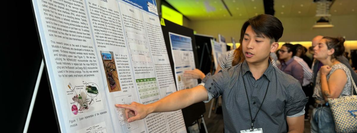 A student points to their poster while discussing their research at Intersections.