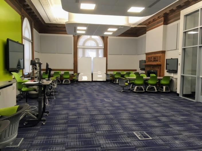 An empty view of Room 101 with several pods of tables and chairs around large-screen monitors.