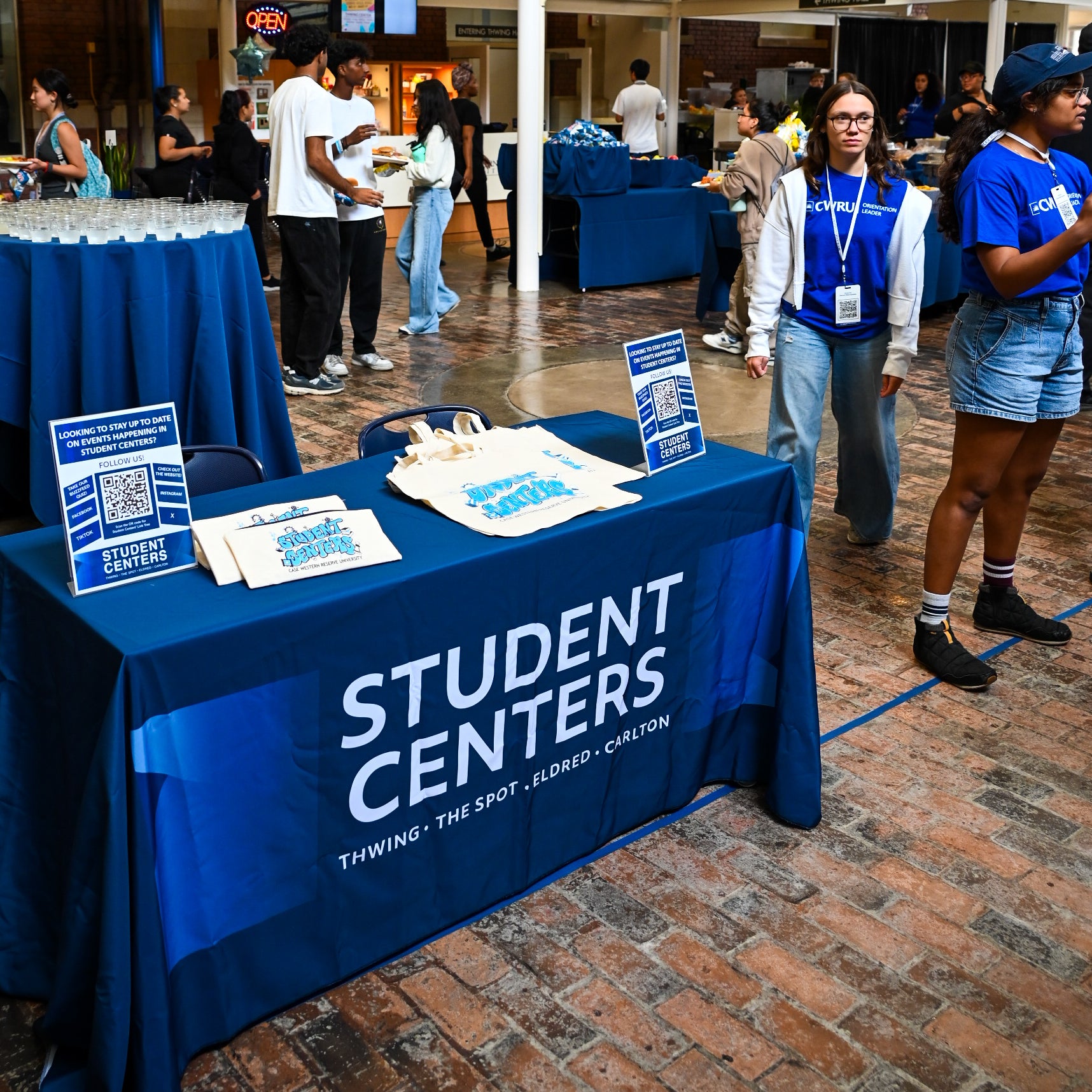 Table with a Student Centers branded table cloth in the atrium with activity around it as the event is starting