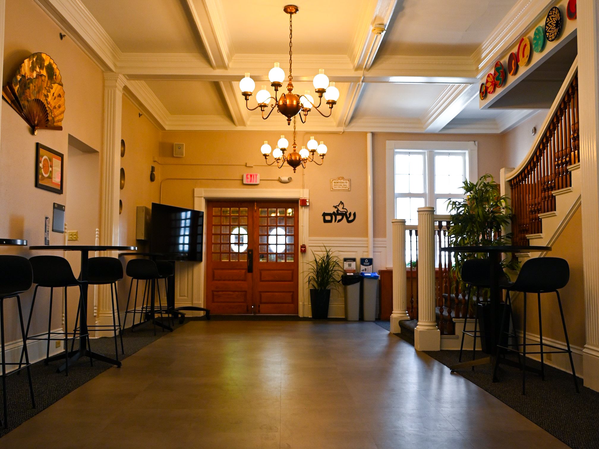 Foyer with hightop tables, and a chandelier hanging from the ceiling and stairway on the right wall