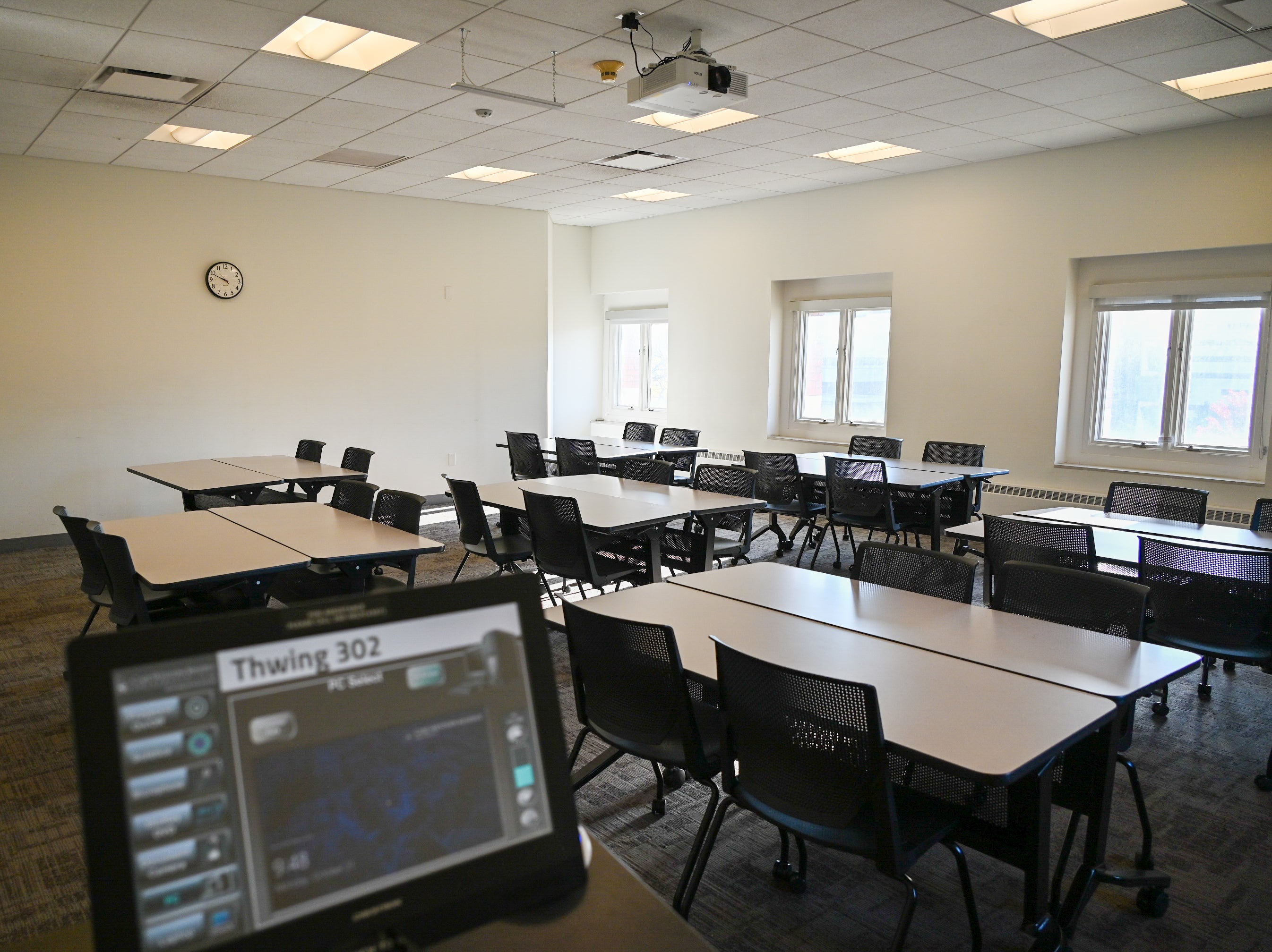 Empty Room 302 in Thwing Center with pods of tables and chairs viewed from the front lectern