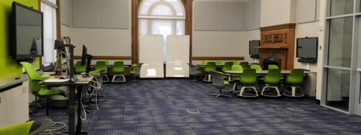 An empty view of Room 101 with several pods of tables and chairs around large-screen monitors.