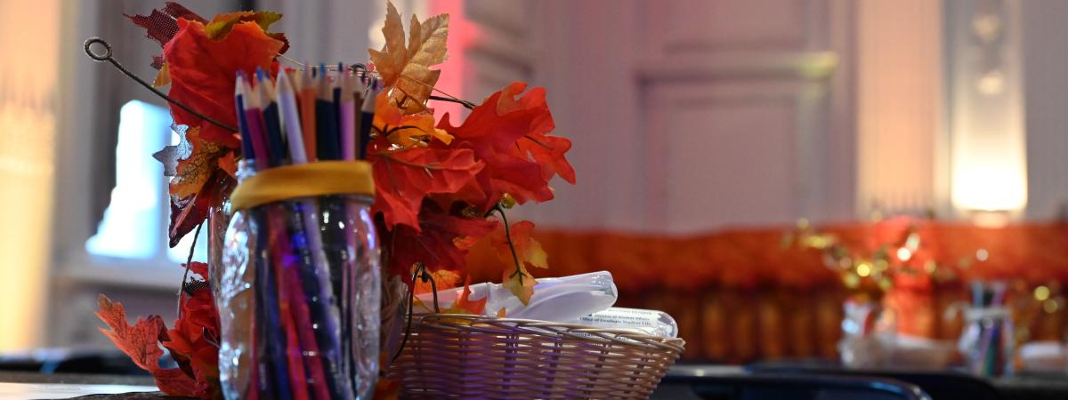 Centerpiece on a table comprised of fall leaves and a mason jar with colored pencils in it