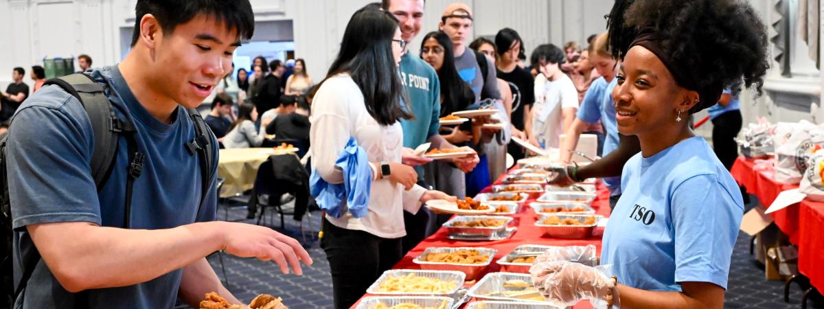 Students smiling while serving food to students as part of an event