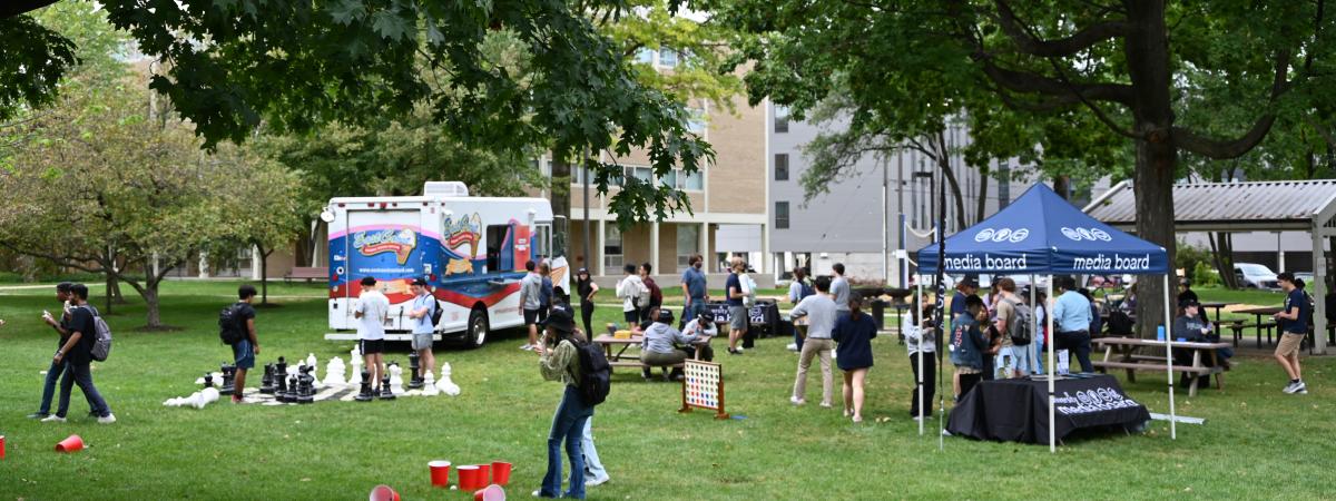 Students mingling and playing games across a field with an ice cream truck and pop up tent