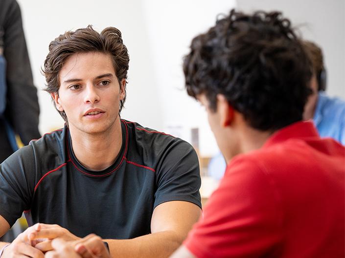 Two male students having a conversation in a classroom setting.