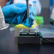 A gloved hand works with precision equipment on a small device.