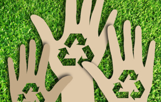 cardboard hands with recycling symbols cut out of them on green grass
